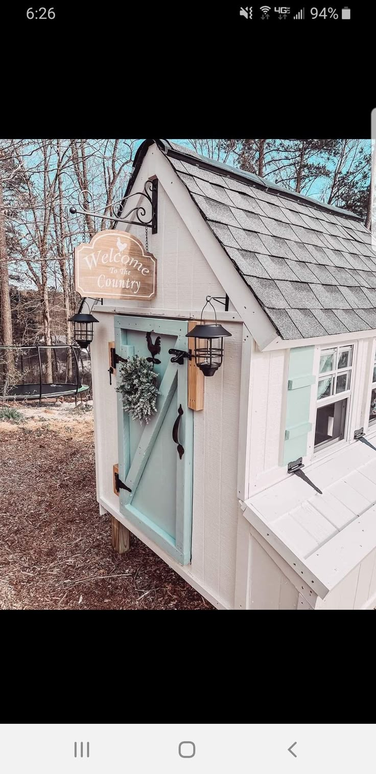 a small white house with a blue door and window on the outside, has a wreath hanging from it's roof