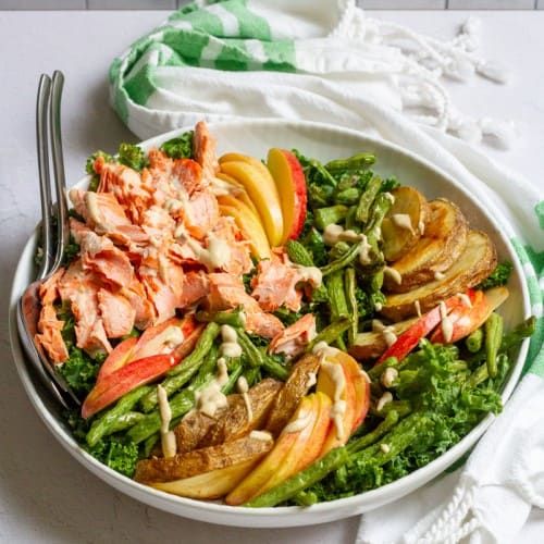 a white bowl filled with lots of food on top of a table next to a fork