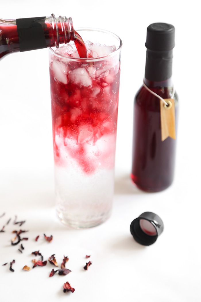 a bottle of wine being poured into a glass filled with ice and cranberries