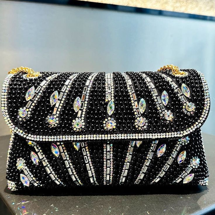 This stunning clutch is embellished with brilliant gem and rhinestone designs, producing a captivating design that catches the light and attention from every aspect. The Luciana Rhinestones Clutch Bag is designed to go well with a variety of ensembles and radiates a classic elegance that elevates any look. It is the ideal piece for special occasions because of its distinctive and striking appearance. For maximum comfort, this bag also includes a gorgeous gold chain strap. Now available in black, Rhinestone Clutch, Floral Heels, Bangle Ring, Bridal Belt, Bridal Bracelet, Rhinestone Designs, Simple Bags, Bridal Jewelry Sets, Bridal Necklace