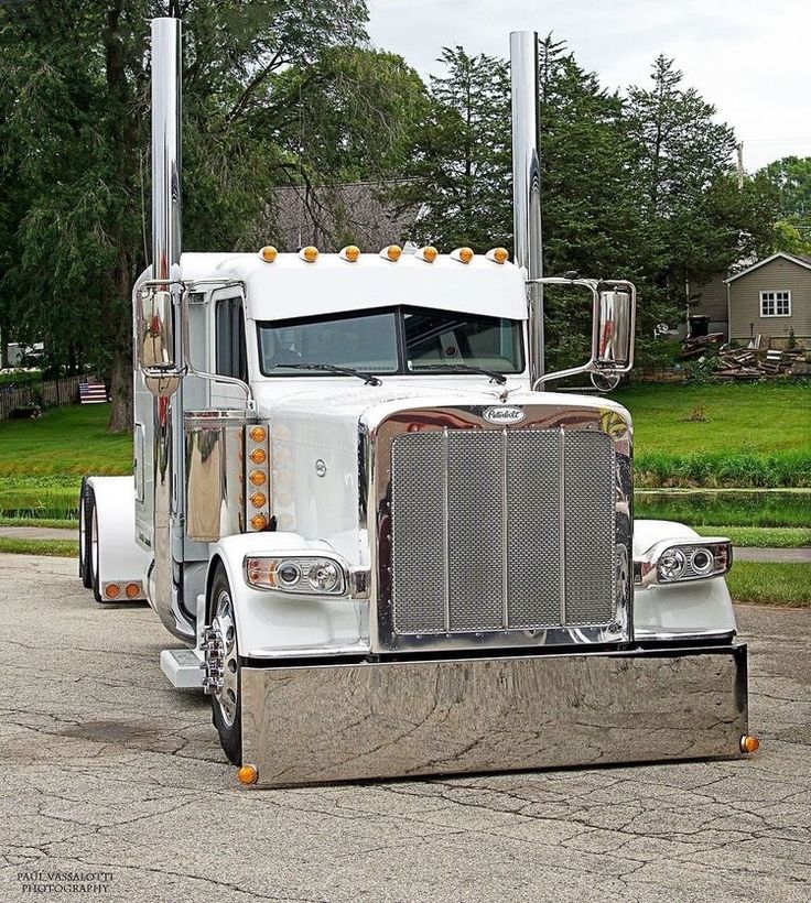 a white semi truck parked in a parking lot next to a green grass covered field