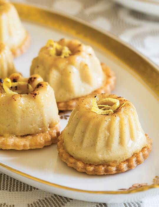 small desserts are sitting on a plate with gold trim around the edges and topped with nuts