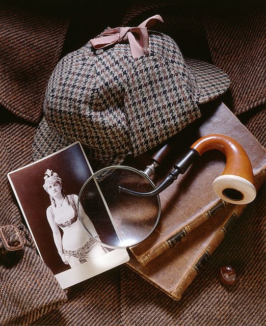 a pair of reading glasses, magnifying glass and book on a brown blanket