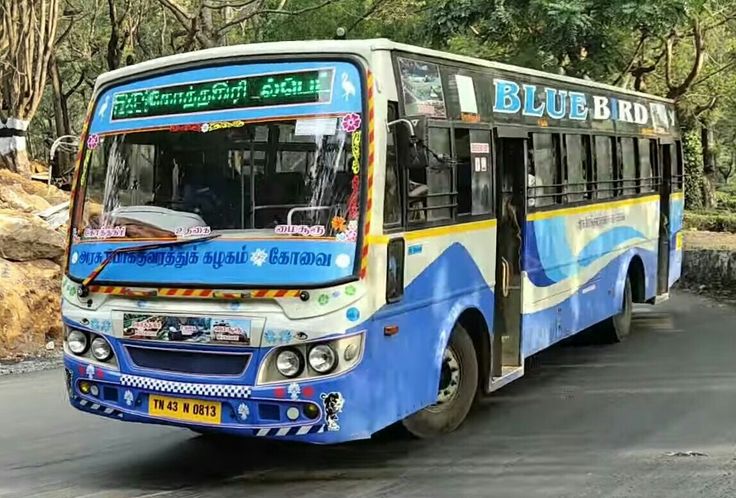 a blue and white bus driving down a street next to some trees in the background