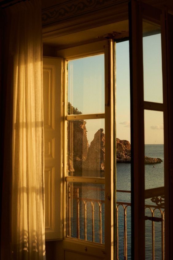 an open window looking out at the ocean and cliffs in the distance with sheer curtains