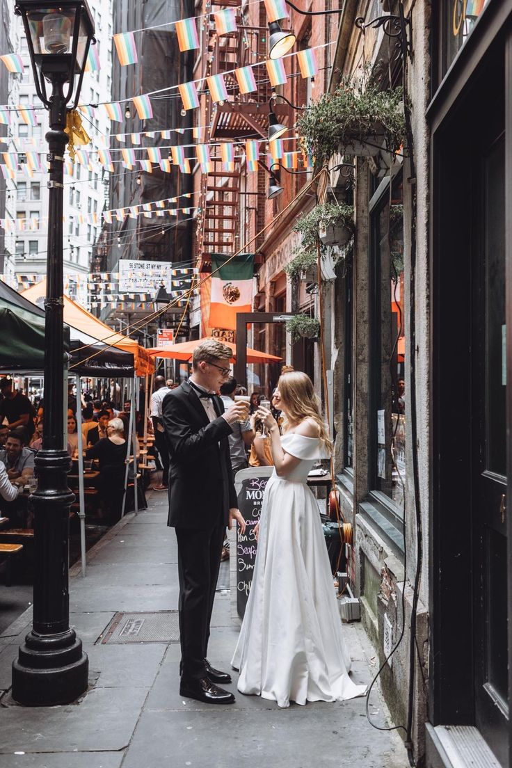 a bride and groom standing in front of a building on a city street with bunting