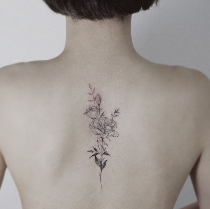 the back of a woman's neck with a flower tattoo on her left shoulder