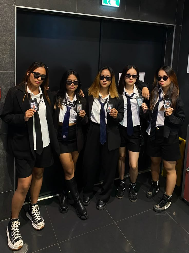 four girls in school uniforms posing for the camera with their thumbs up and sunglasses on