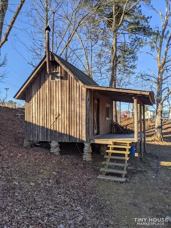 a small wooden cabin in the woods with stairs leading up to it's roof