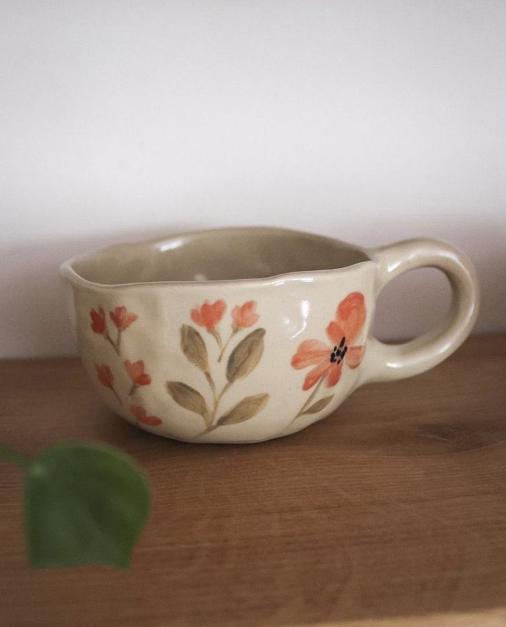 a white bowl with flowers painted on it sitting on a table next to a plant