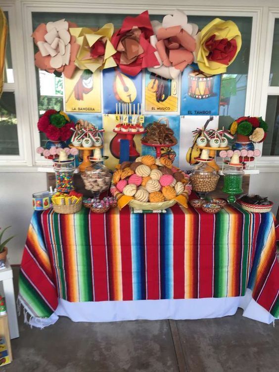 a colorful table covered in lots of food next to a wall with pictures on it