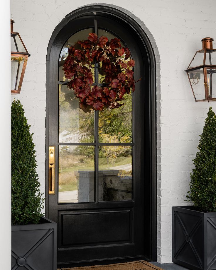 a black front door with a wreath and two planters on either side of it