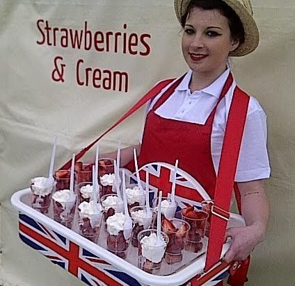 a woman in an apron holding a tray of strawberries and creams on sticks