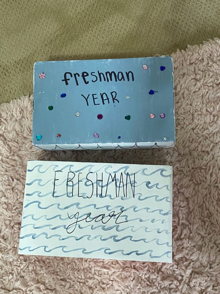 two boxes with writing on them sitting on a bed next to each other, one has a sign that says freshmon year and the other reads ebersman jones