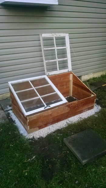 an old window is sitting in the grass next to a shed with snow on it