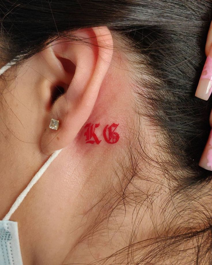 a woman with red ink on her left ear and behind her ear is a tattoo that reads k c