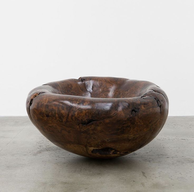 a large wooden bowl sitting on top of a cement floor next to a white wall