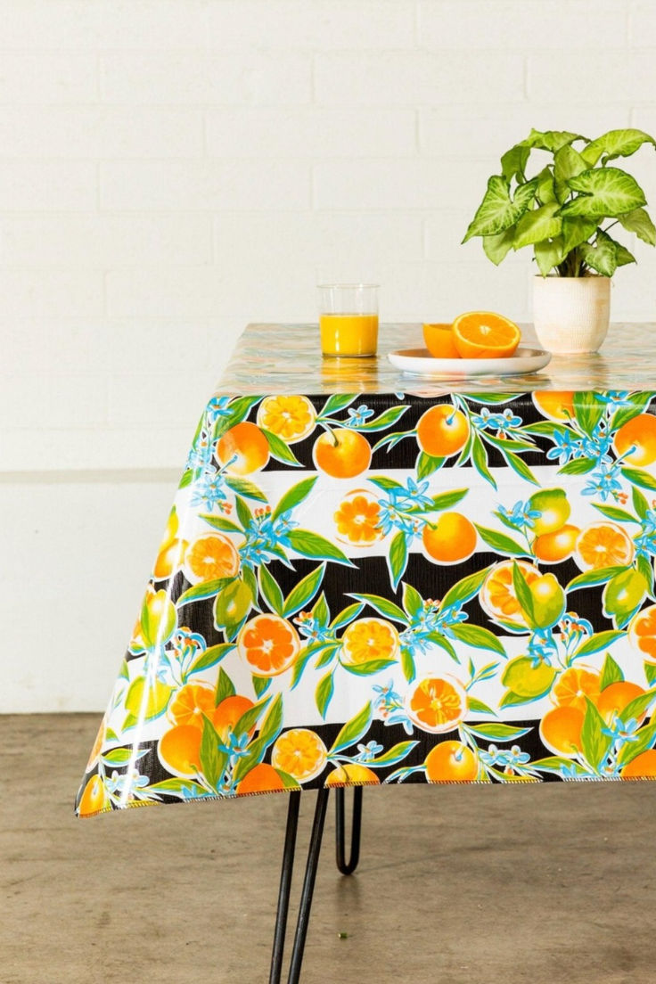 an orange print tablecloth on a black and white patterned table cloth with two small plant in the background