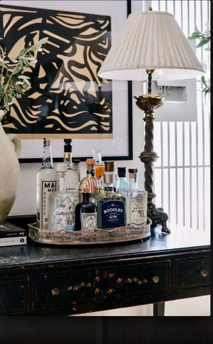 a table topped with lots of liquor bottles and glasses next to a lamp on top of a dresser