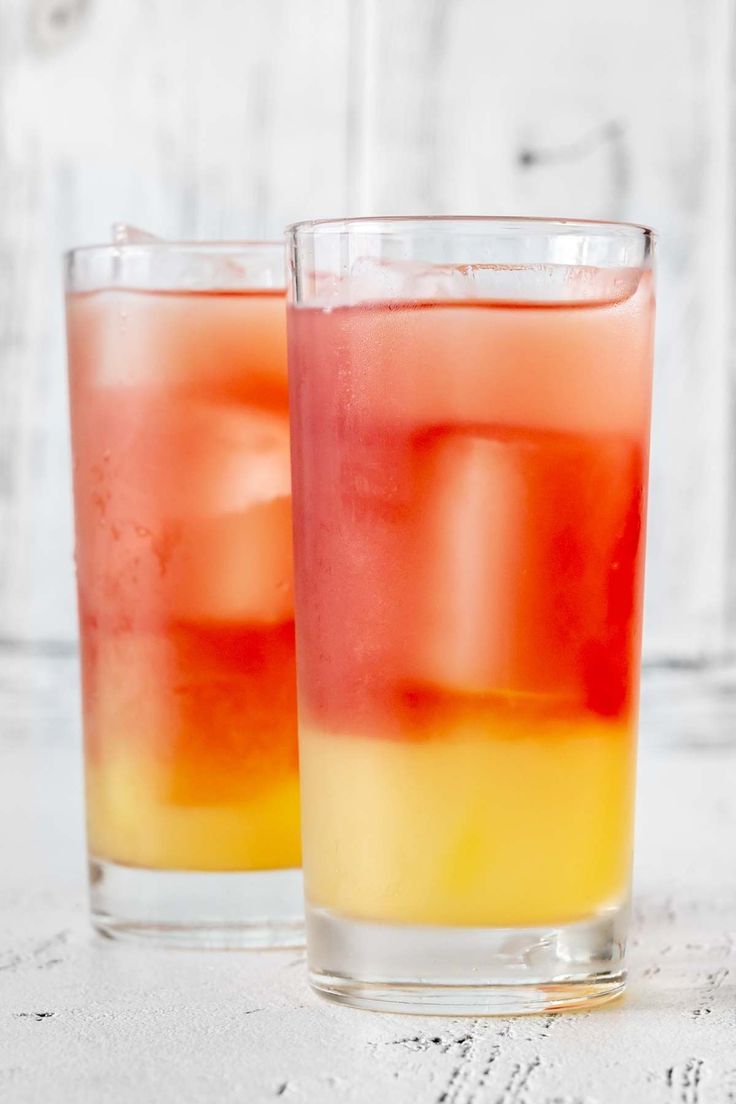 two glasses filled with different colored drinks on top of a white tableclothed surface