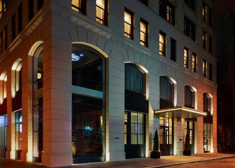 an empty street at night in front of a building with lit up windows and shutters