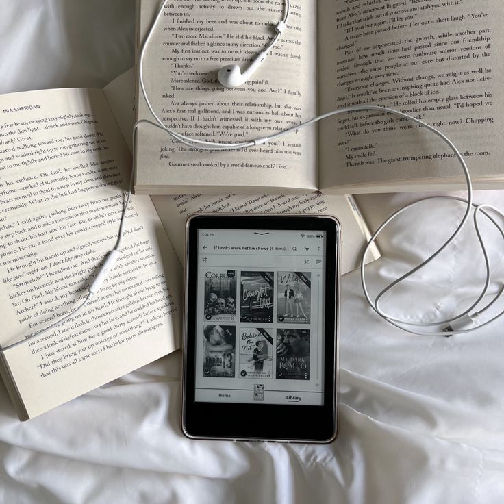 an electronic device sitting on top of a bed next to two open book's