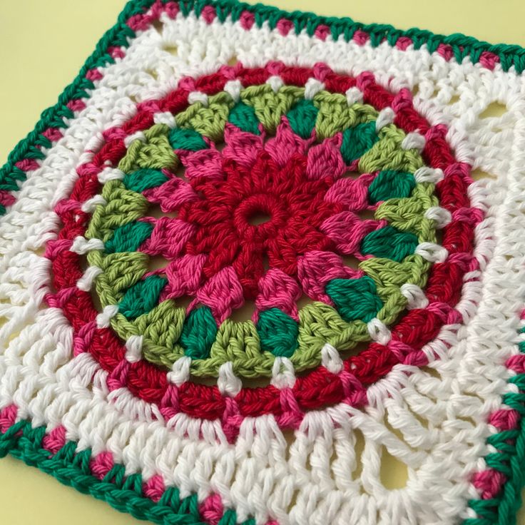 a crocheted square with green, red and white colors on it sitting on a table