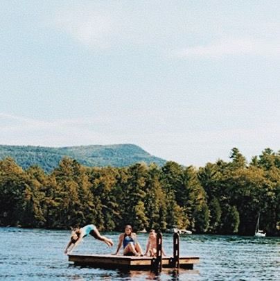 three people are sitting on a dock in the water and one person is diving into the lake