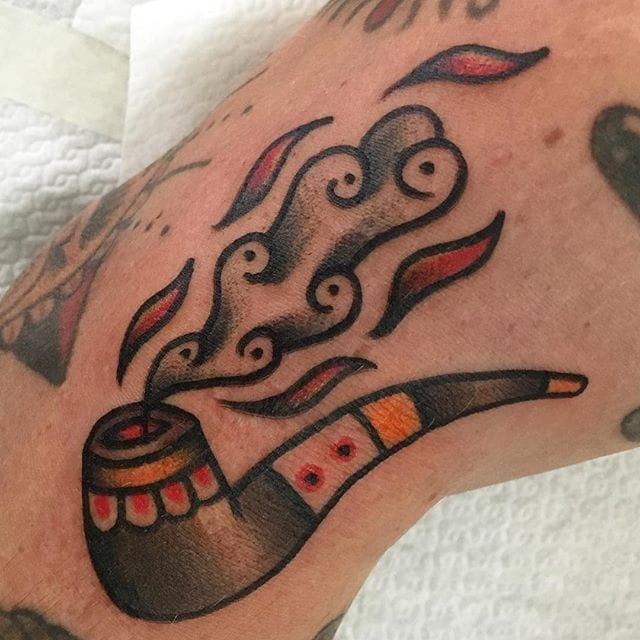 a close up of a person's arm with tattoos on it and a pipe