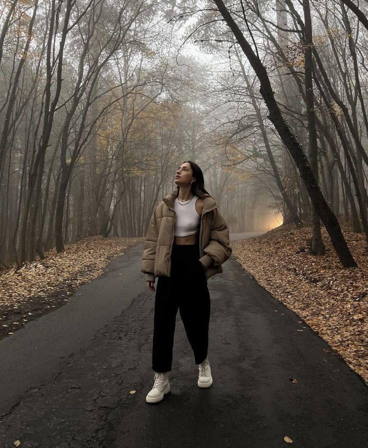 a woman standing in the middle of a road with trees and leaves all around her