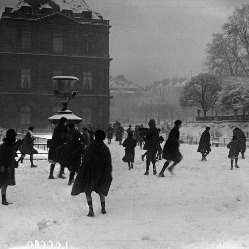 many people are walking in the snow near a building with a light pole on top