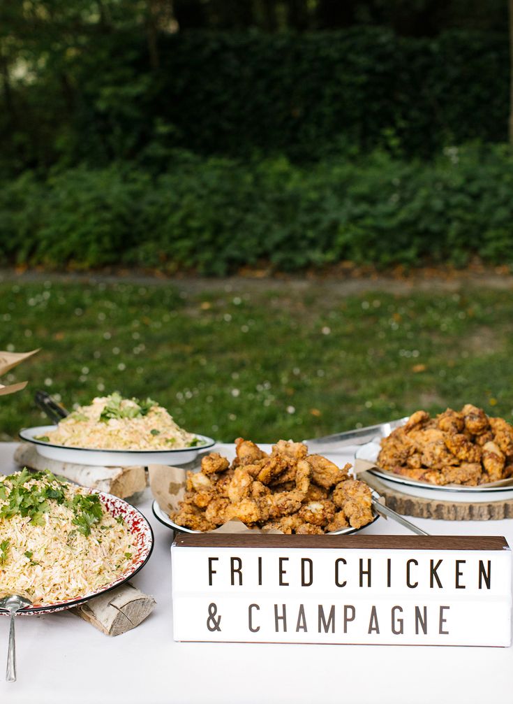 fried chicken and champagne are on display at the outdoor buffet table in front of some trees