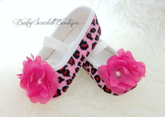 pair of pink and black baby shoes with flowers on the bottom, sitting on white fur