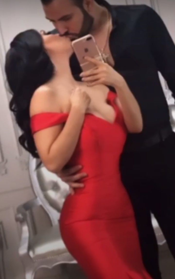 a woman in a red dress and a man in a black suit kissing her on the cheek