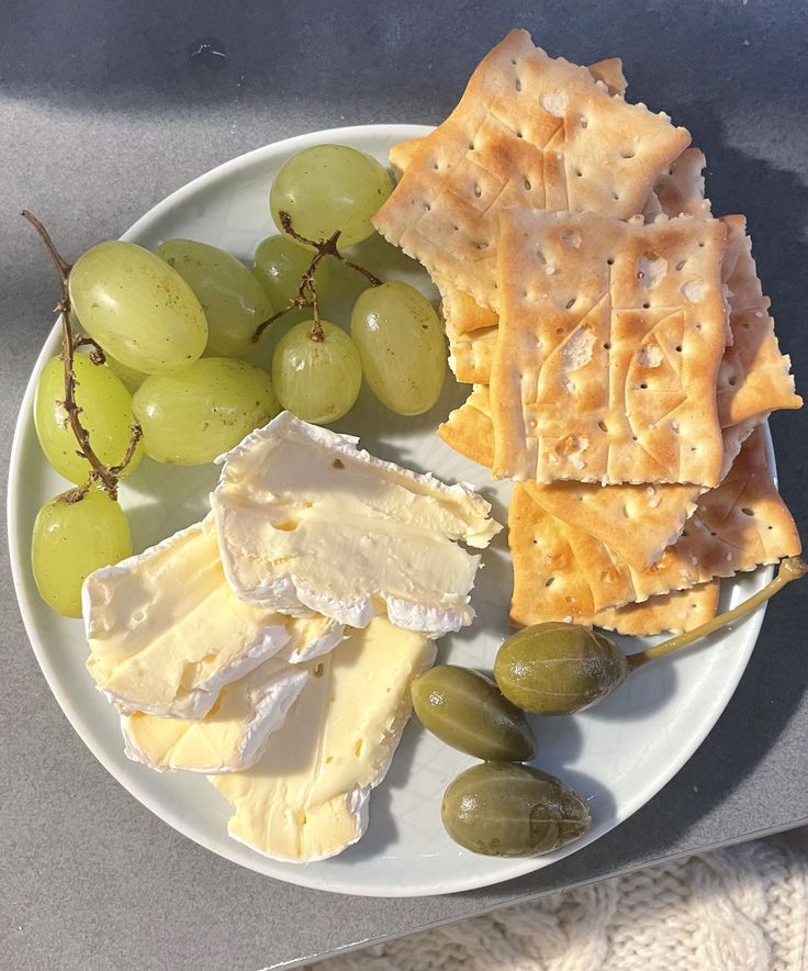 a white plate topped with cheese and crackers next to green grapes on a table