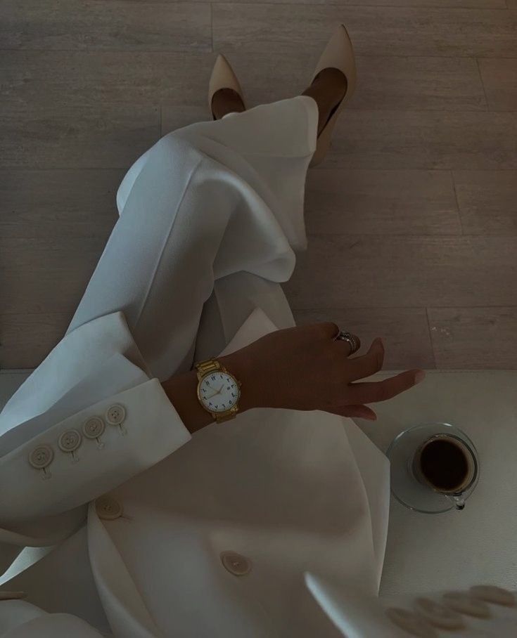 a woman in white is sitting at a table with a cup of coffee and watch