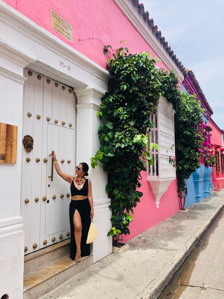 a woman leaning up against a pink and white building with ivy growing on the wall