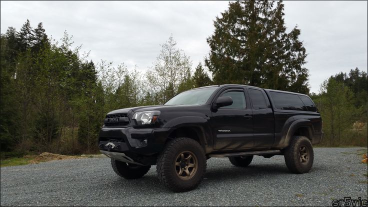 a black truck parked on top of a gravel road next to some trees and bushes