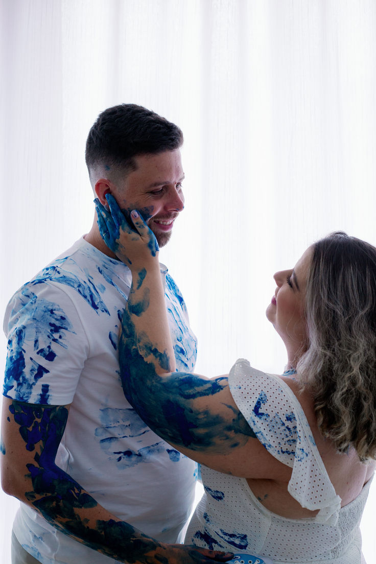 a man and woman with blue paint on their arms talking on the phone together in front of a white curtain