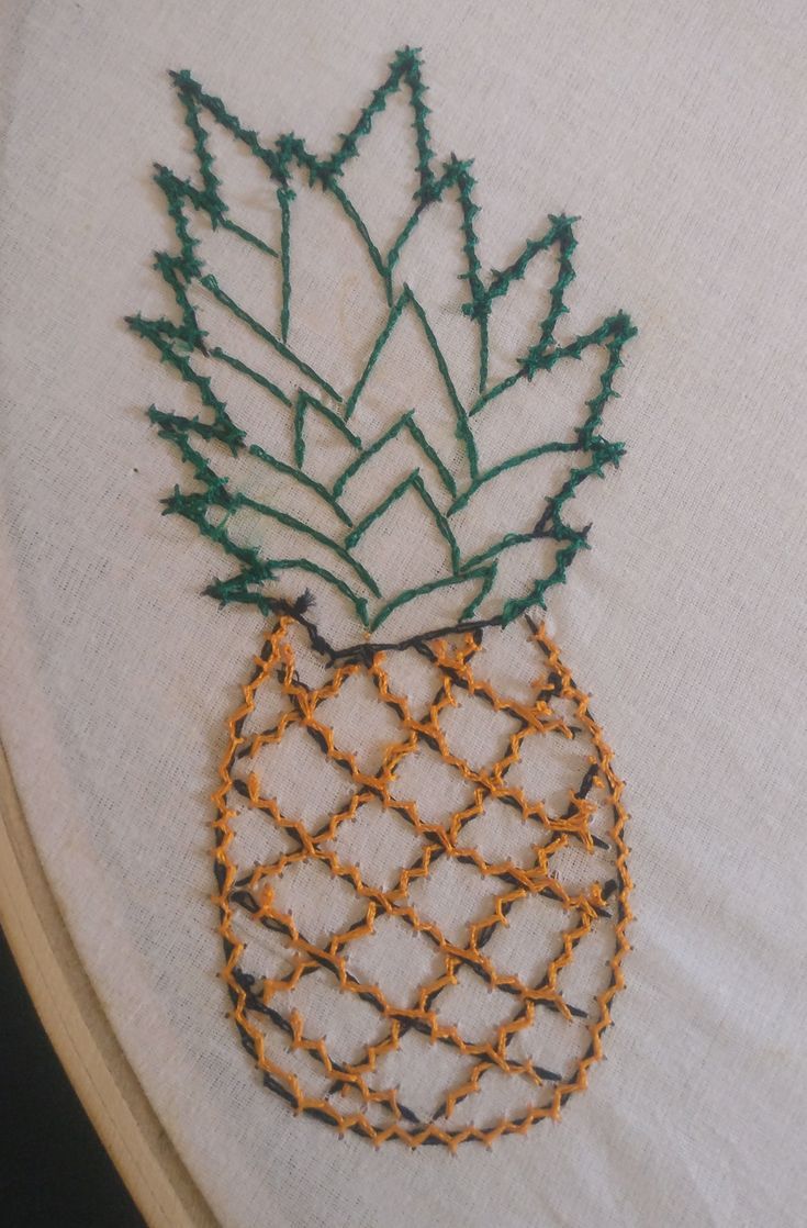 an embroidered pineapple on a white piece of cloth with orange and green trimmings