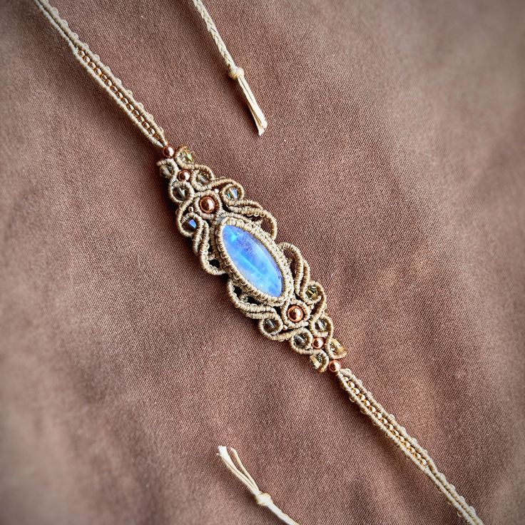 a gold chain with a blue stone in the center on a brown velvet cloth background