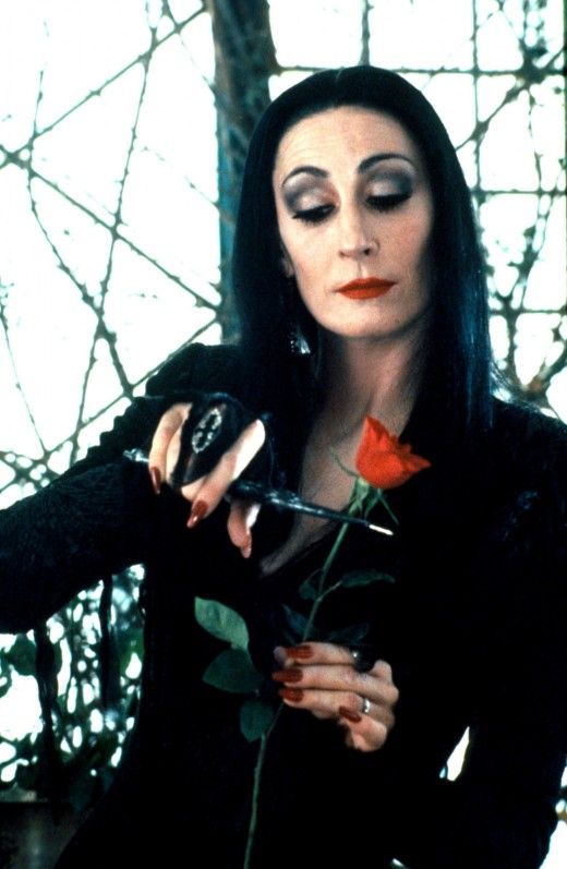 a woman with black hair and makeup holding a rose in her right hand while looking at the camera