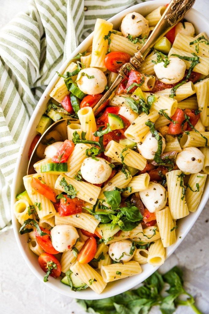 a white bowl filled with pasta salad and garnished with parsley on the side