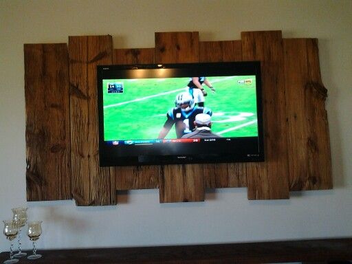 a flat screen tv mounted to the wall above a wooden shelf with wine glasses on it