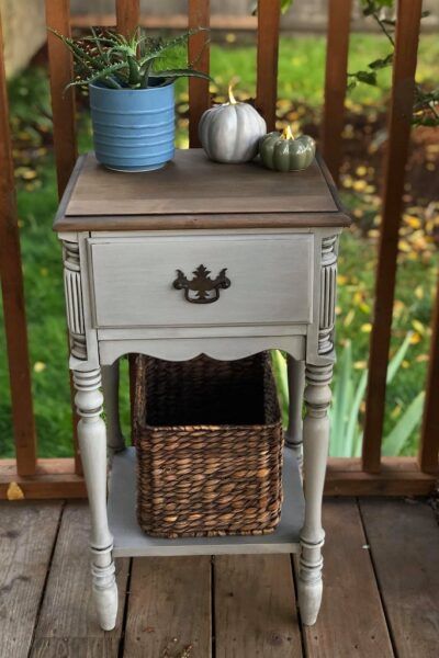 a small table with a basket on top of it and two pumpkins sitting next to it