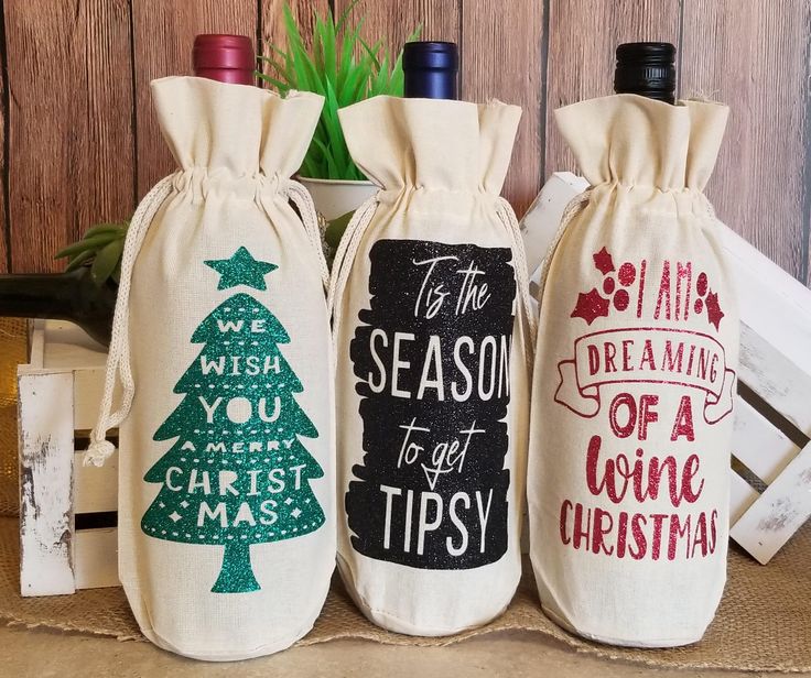 three wine bags with christmas sayings are sitting on a table next to some bottles