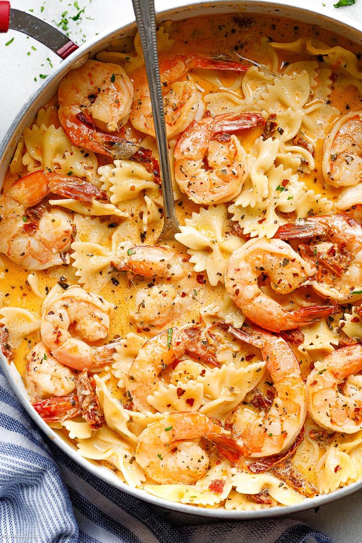 a skillet filled with pasta and shrimp on top of a blue towel next to a fork