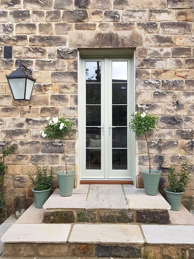 two potted plants sit on the steps in front of a stone building with a glass door