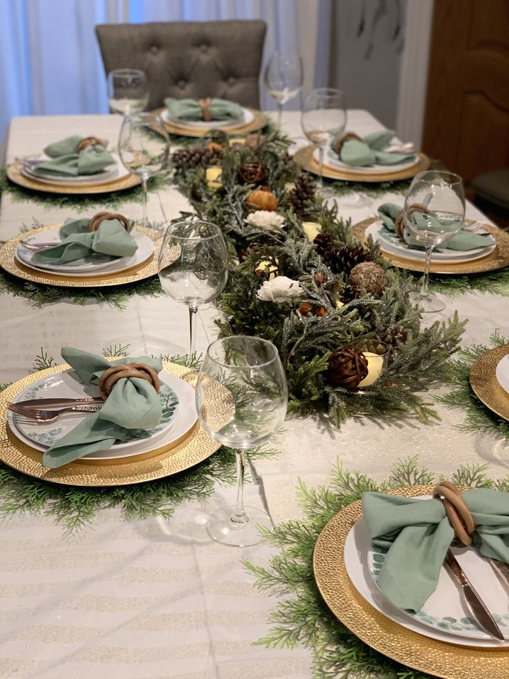 the table is set for christmas dinner with pine cones and greenery