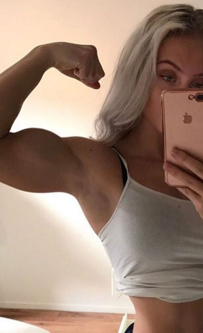 a woman taking a selfie in the mirror with her cell phone and showing off her muscles